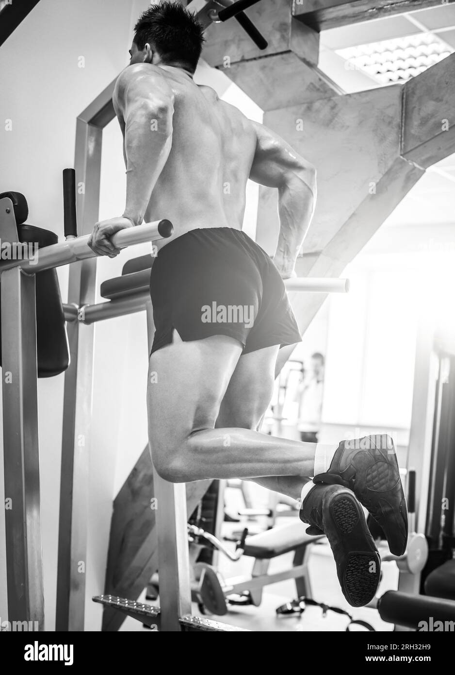 Strong bodybuilder doing exercises triceps push-ups on a parallel bars in a modern gym Stock Photo