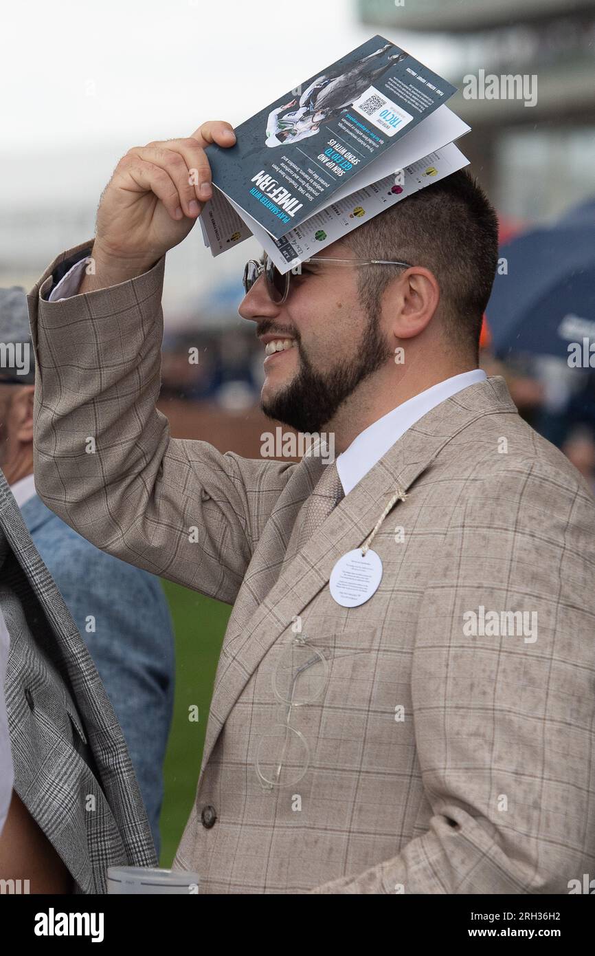 Ascot, Berkshire, UK. 12th August, 2023. A man shelters from the rain ...