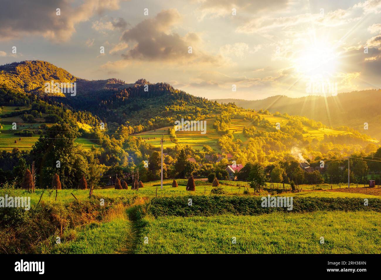 mountainous rural landscape in summer at sunset. village in the valley with haystacks on the hillside near forest. beautiful countryside scenery of uk Stock Photo