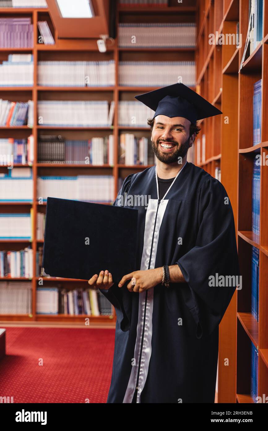 Excited graduate wearing a cap and gown holding his bachelor's degree ...