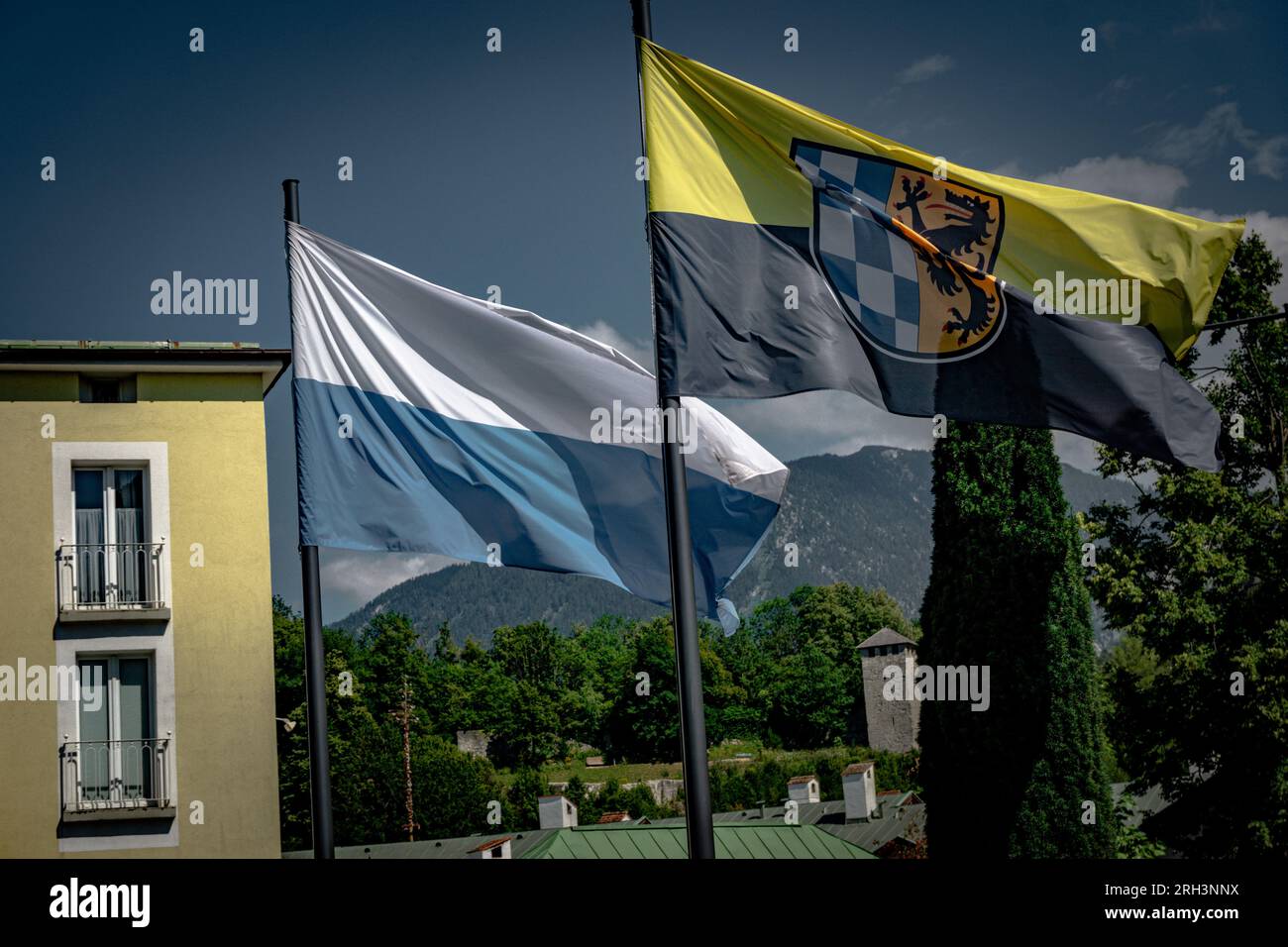 Bavarian and Bavarian munich flags stand right next to each other and wave tautly in the wind. The mountains of Bavaria and the blue cloudy sky Stock Photo