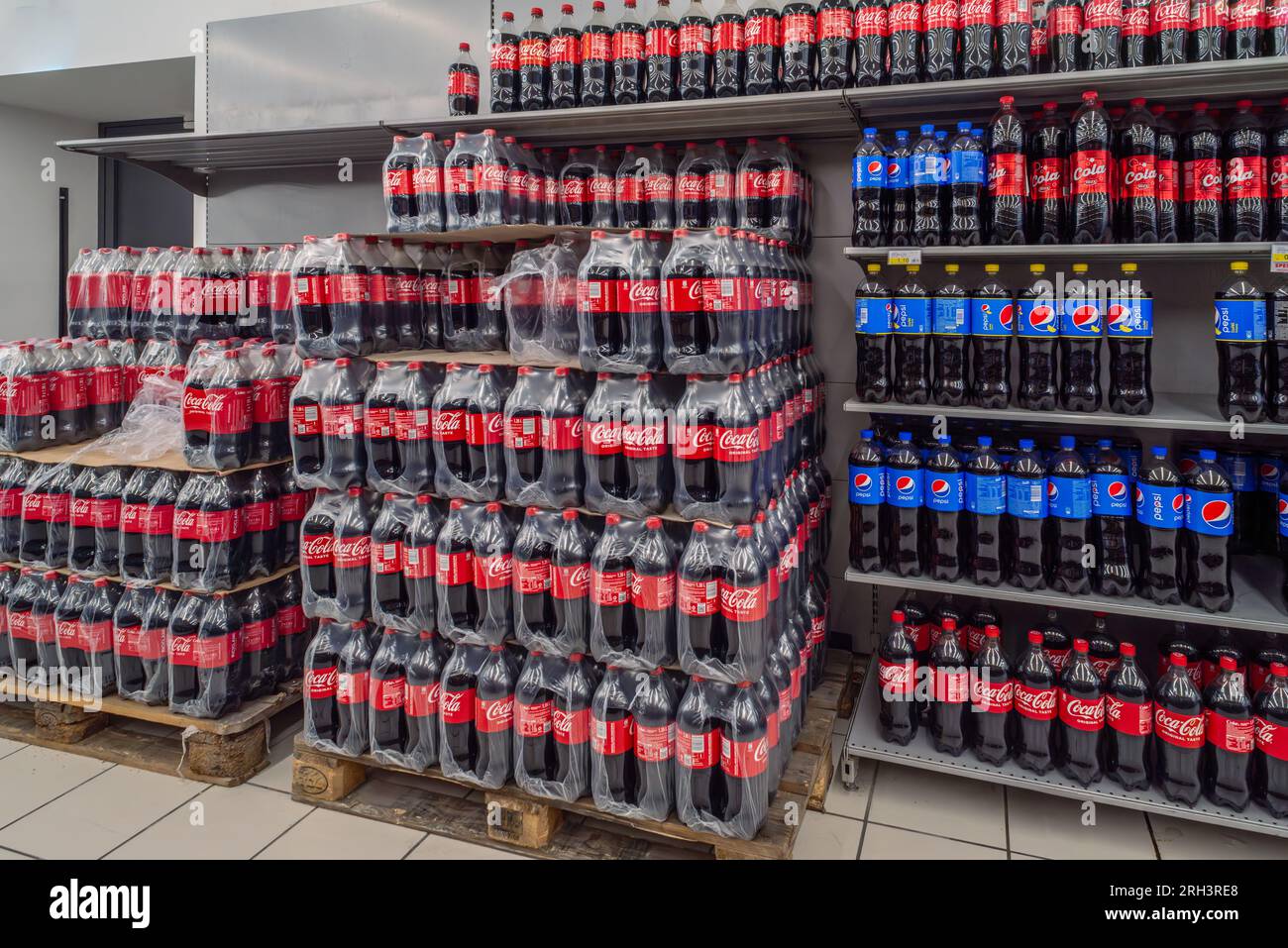 Italy - August 08, 2023: Coca Cola in plastic bottles packed in plastic film and stacked on pallets and Pespi bottle on shelf for sale in Italian stor Stock Photo