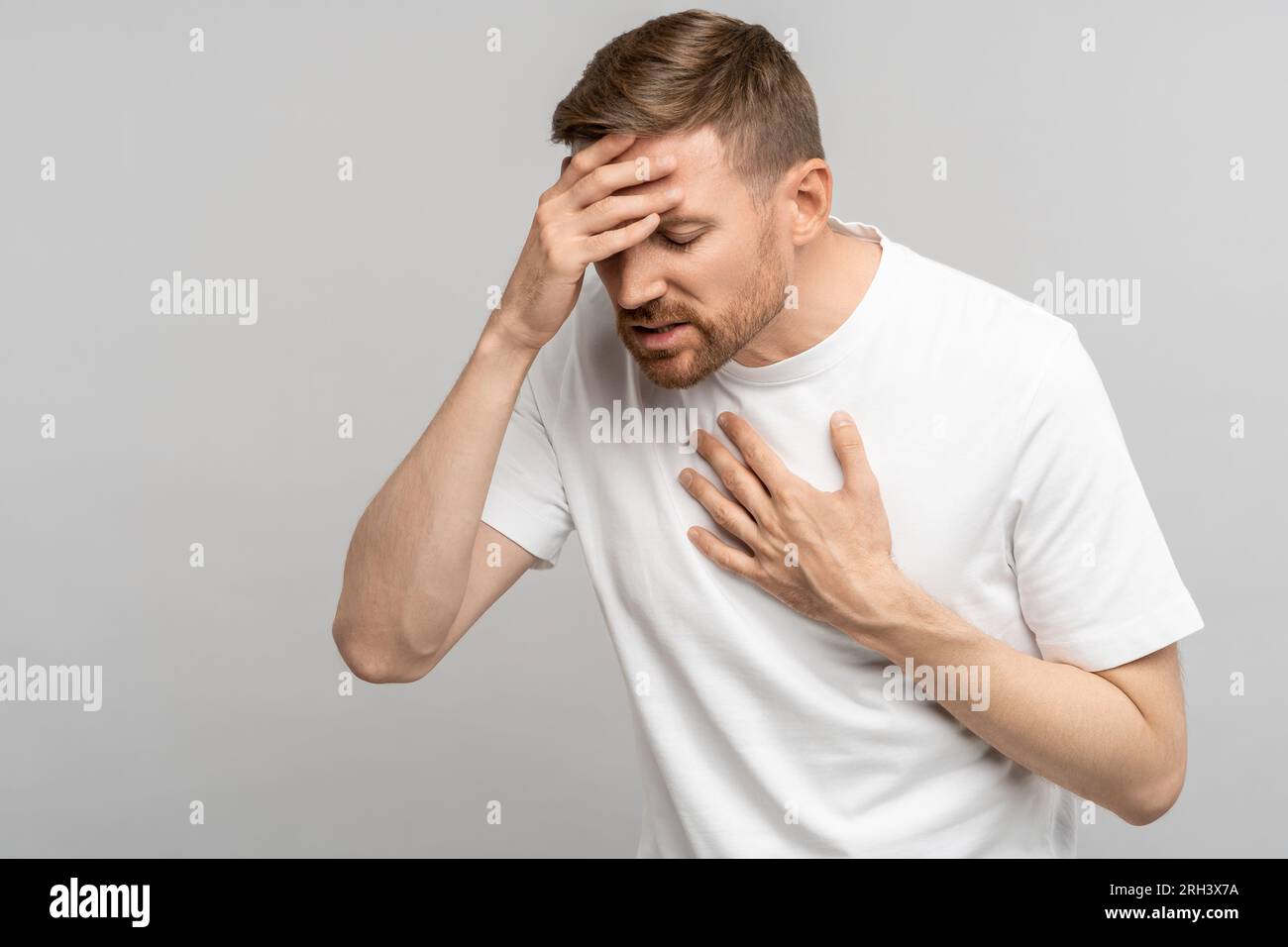 Unhealthy middle aged man presses hand to chest and head having heart pain, headache, dizziness Stock Photo