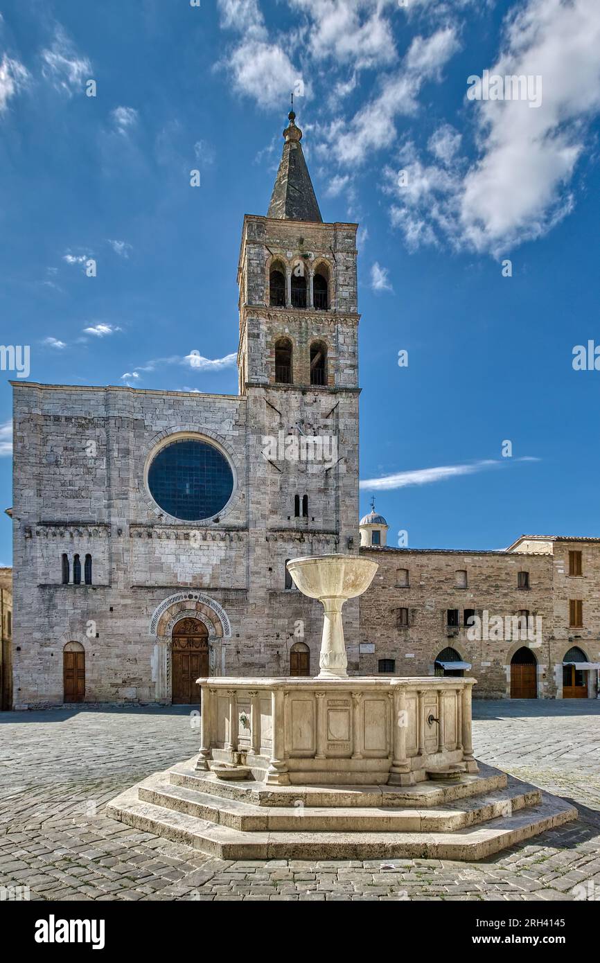 Town of Bevagna, Umbria, Italy. The 19th century fountain and 12th century St Michael's Church in Piazza Silvestri with blue sky and white clouds. Stock Photo