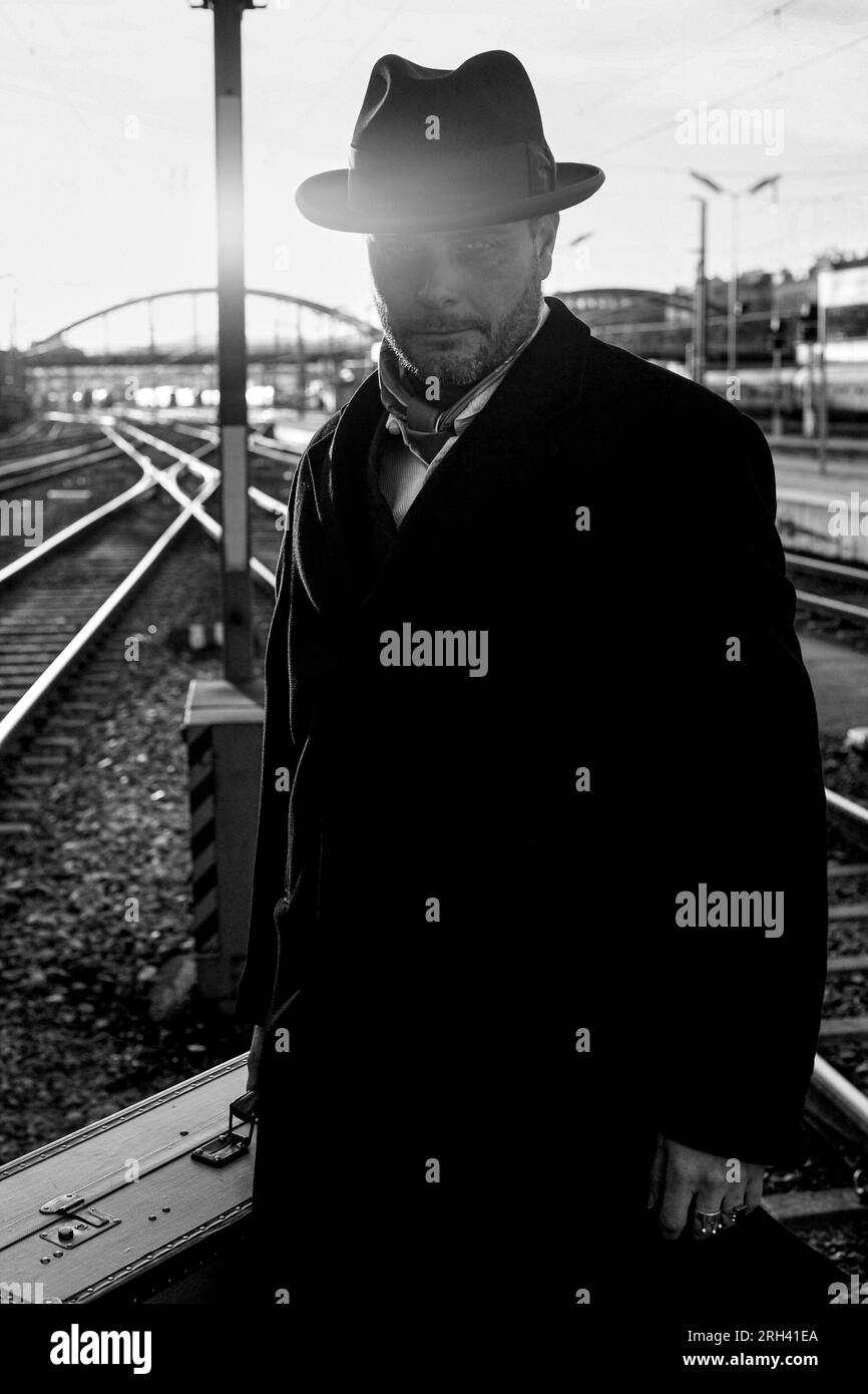 Man in coat is waiting for a train on station platform between the tracks in early morning hours. Stock Photo
