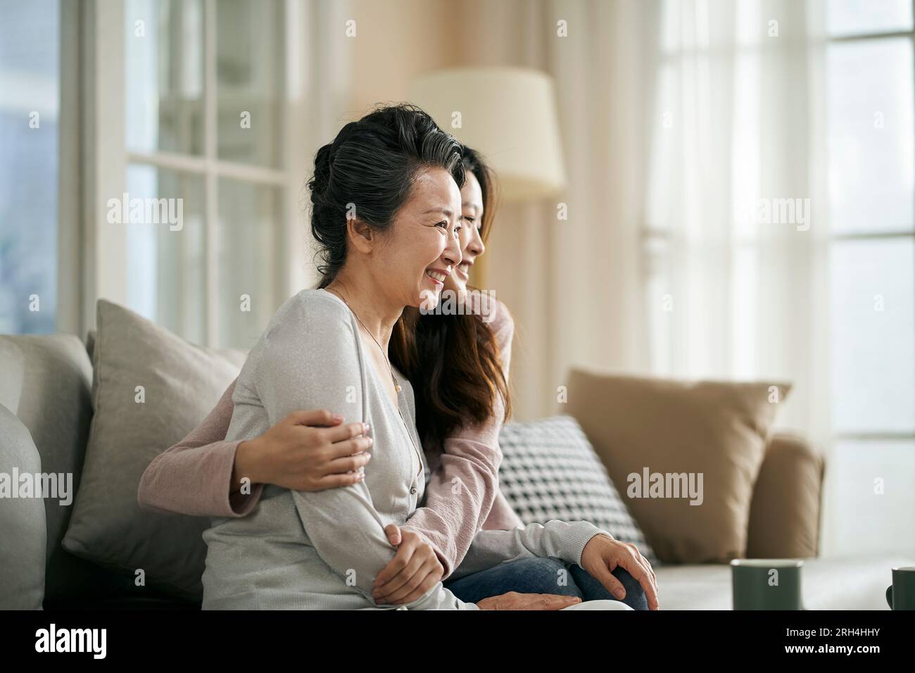 portrait of asian elderly mother and adult daughter sitting on couch at home happy and smiling Stock Photo