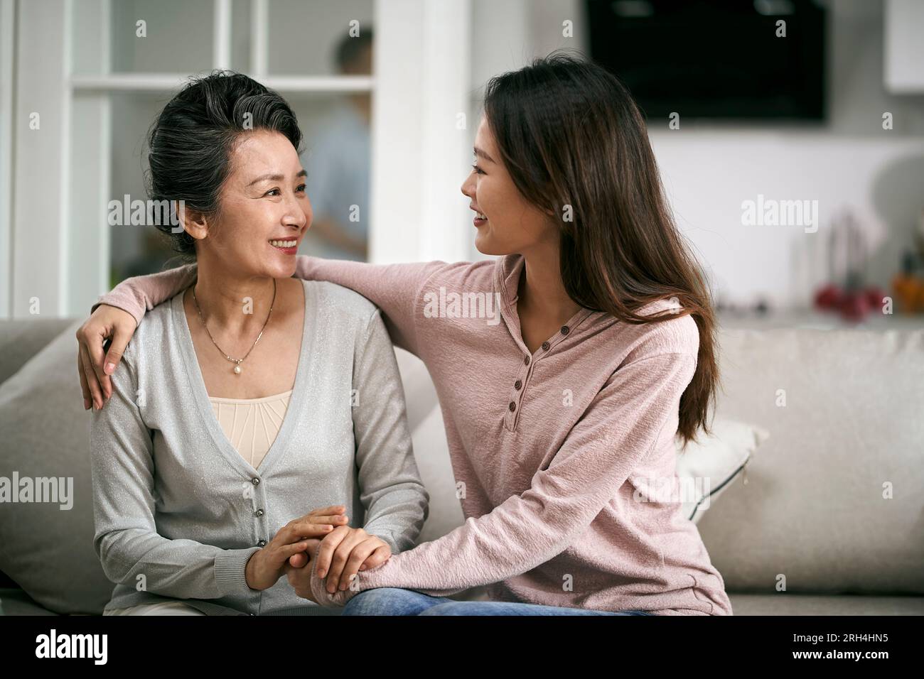 asian adult daughter and senior mother sitting on couch at home having a pleasant conversation Stock Photo