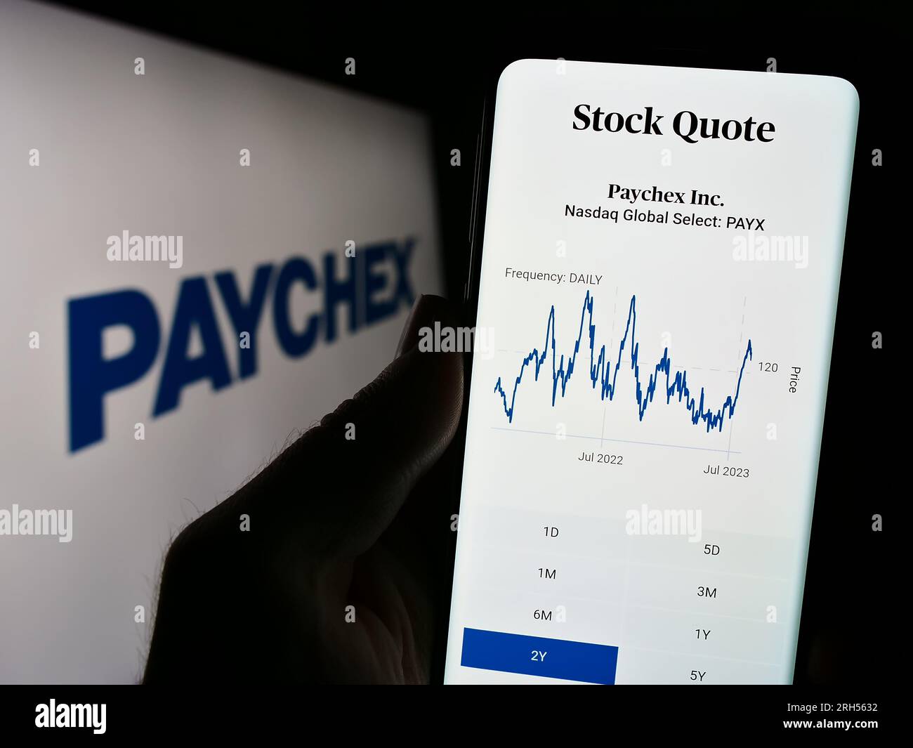 Person holding cellphone with website of US outsourcing company Paychex Inc. on screen in front of logo. Focus on top-left of phone display. Stock Photo