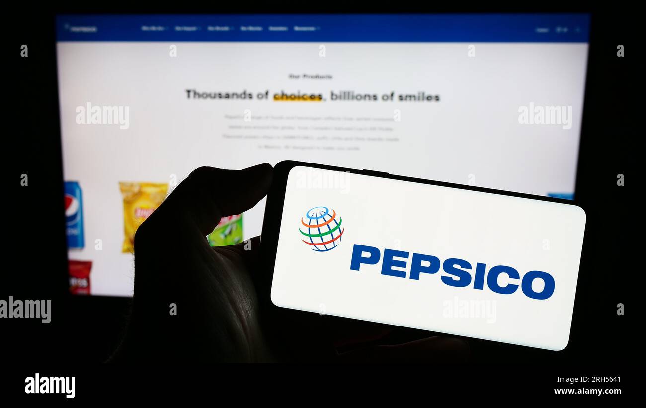 Person holding smartphone with logo of US beverage and snack company PepsiCo Inc. on screen in front of website. Focus on phone display. Stock Photo