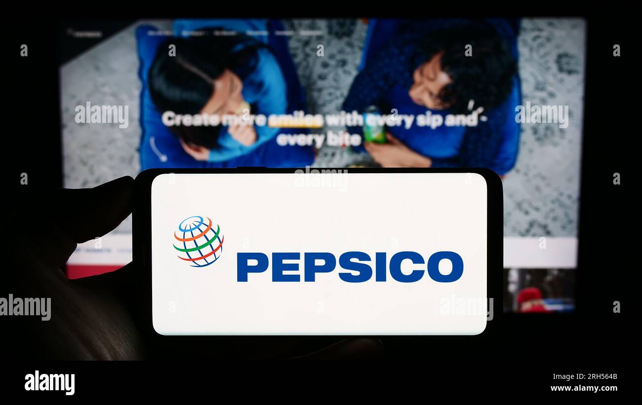 Person holding cellphone with logo of US beverage and snack company PepsiCo Inc. on screen in front of business webpage. Focus on phone display. Stock Photo