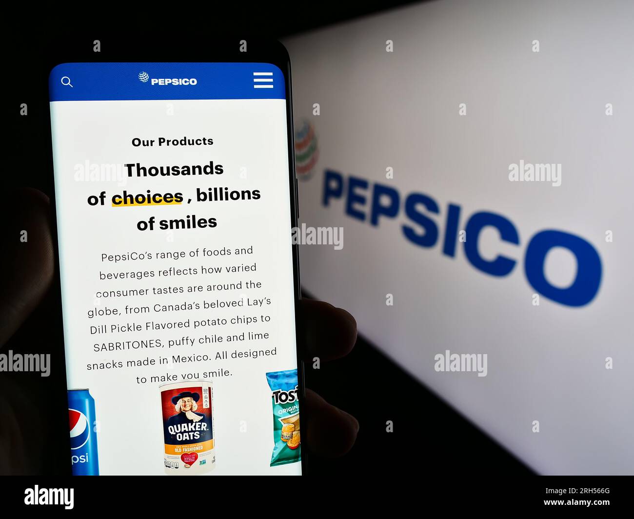 Person holding cellphone with webpage of US beverage and snack company PepsiCo Inc. on screen in front of logo. Focus on center of phone display. Stock Photo