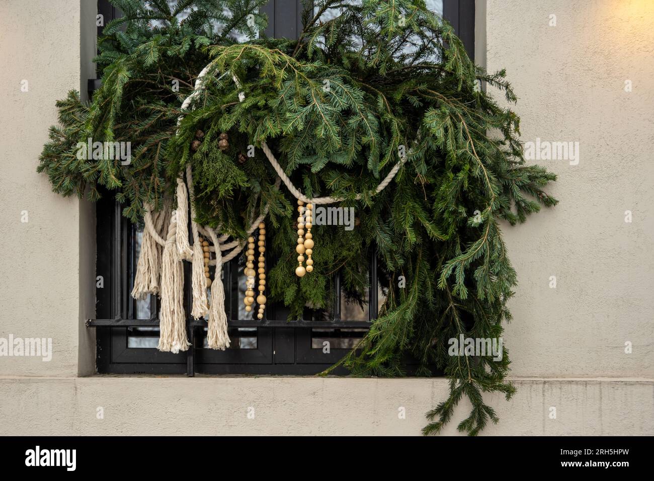 Christmas window decoration. Branches of a blue spruce with cones and a garland hanging on the window of the house. Home decoration for Christmas and Stock Photo
