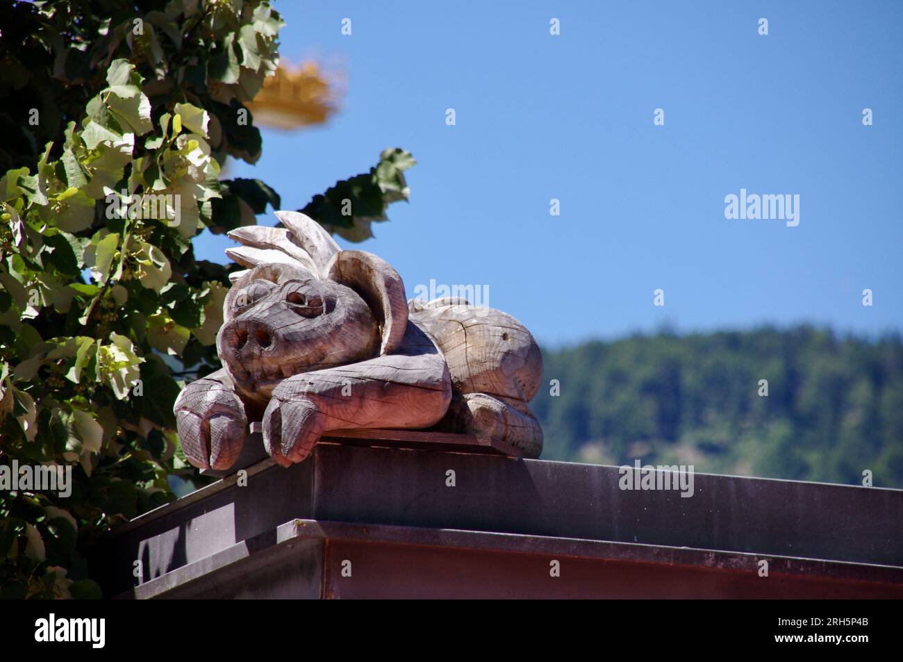 Little wooden carved pig looking over a wall with blue sky behind. Stock Photo