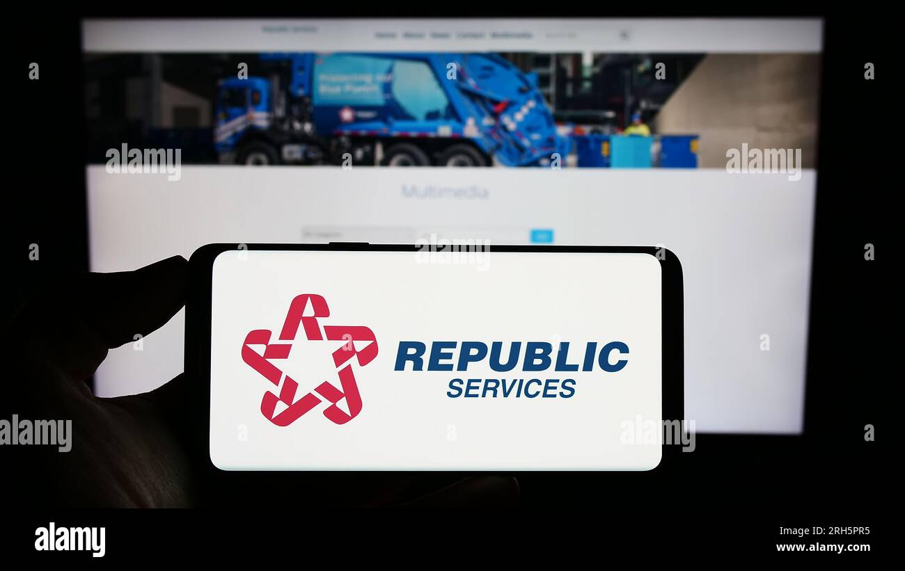 Person holding cellphone with logo of US waste disposal company Republic Services Inc. on screen in front of webpage. Focus on phone display. Stock Photo