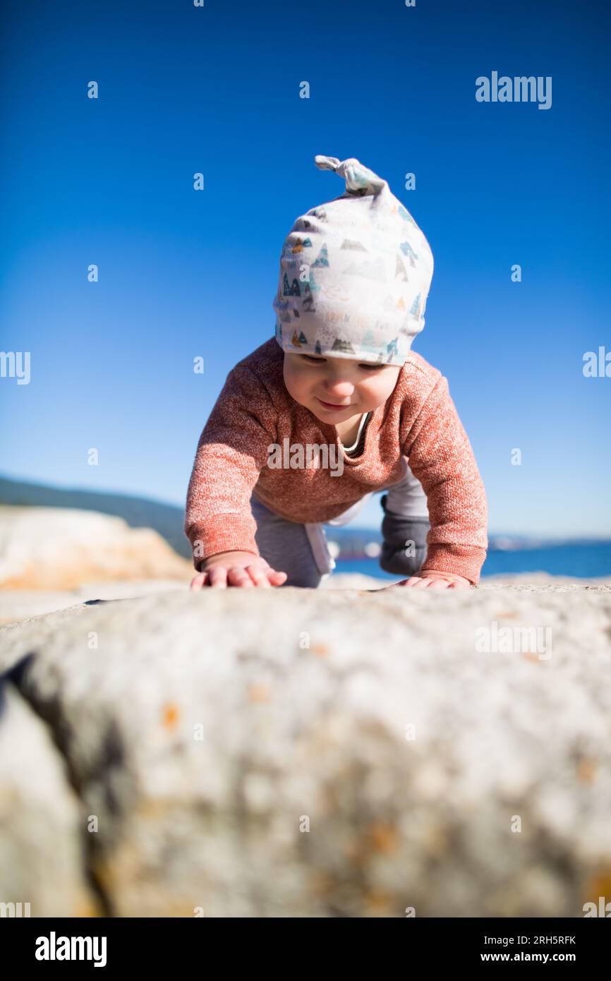 Baby crawling on shoreline rocks, sunny day. Stock Photo