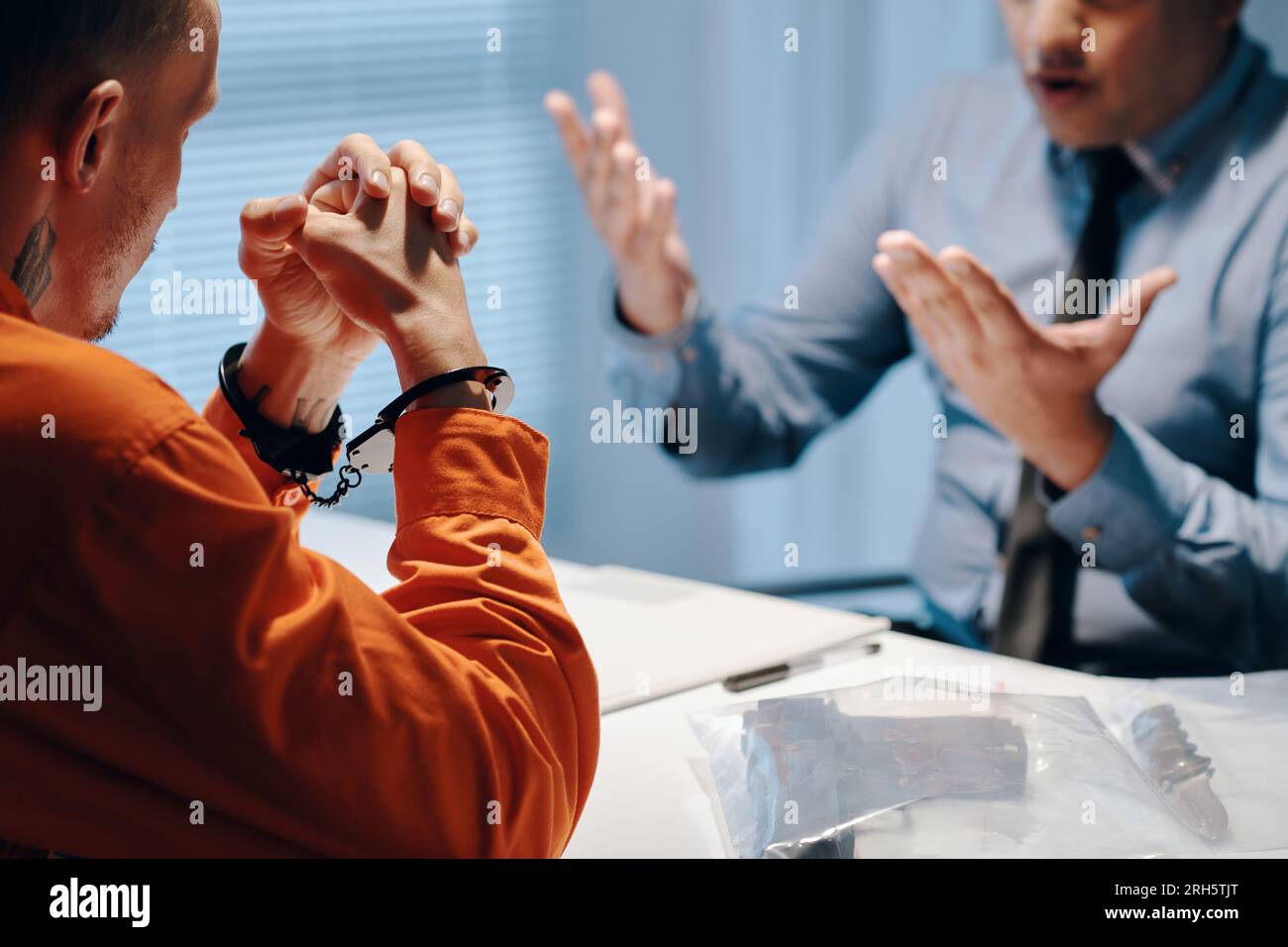 Criminal in handcuffs talking to policeman in interrogation room Stock