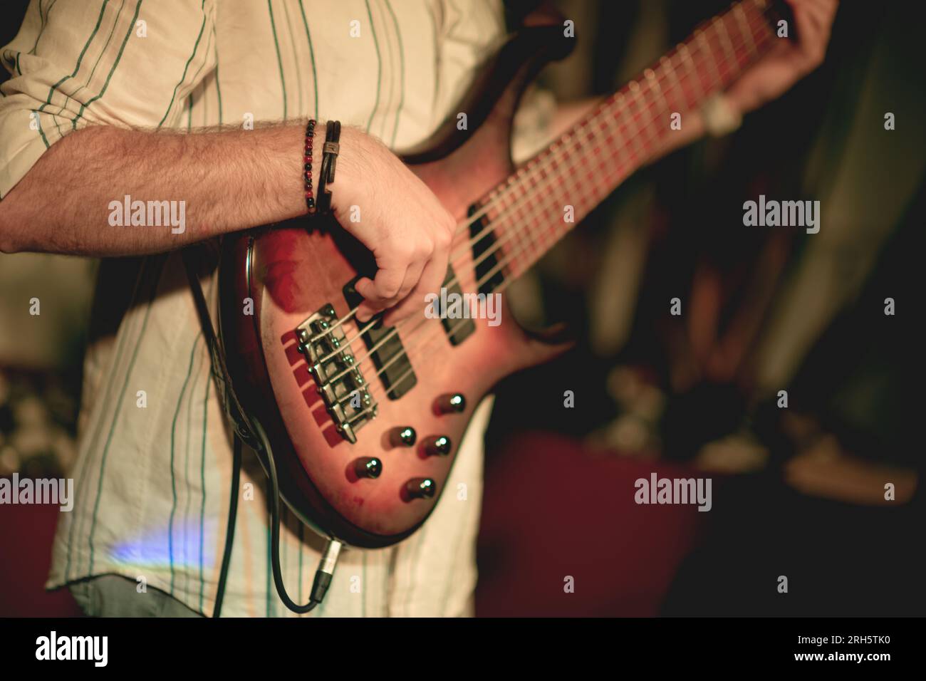 A close-up shot of a bass guitar being played by a young man in his twenties. The focus is on the instrument, with the player's face not visible, emph Stock Photo