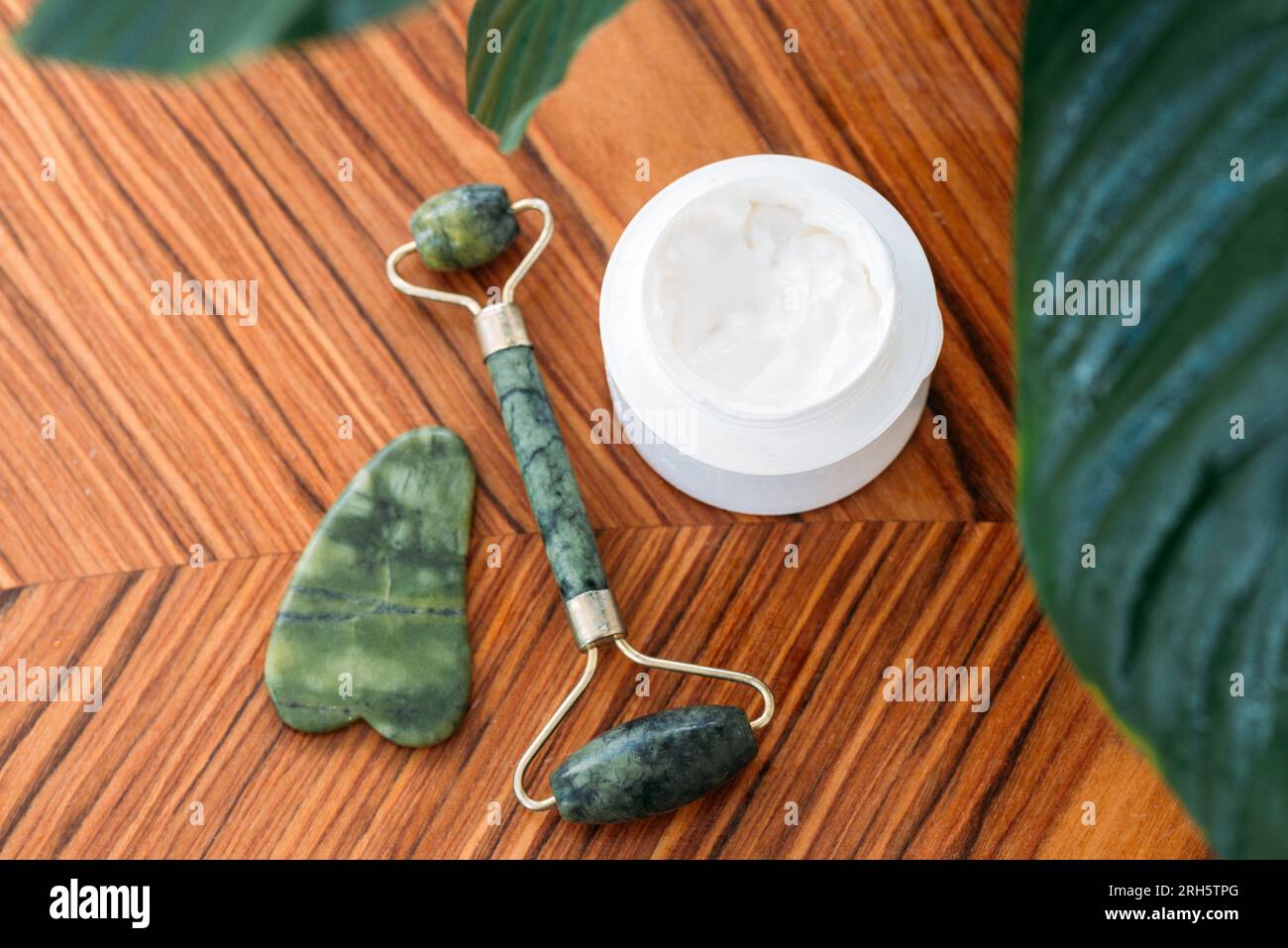 gouache roller, and stone with face cream on wooden background, top