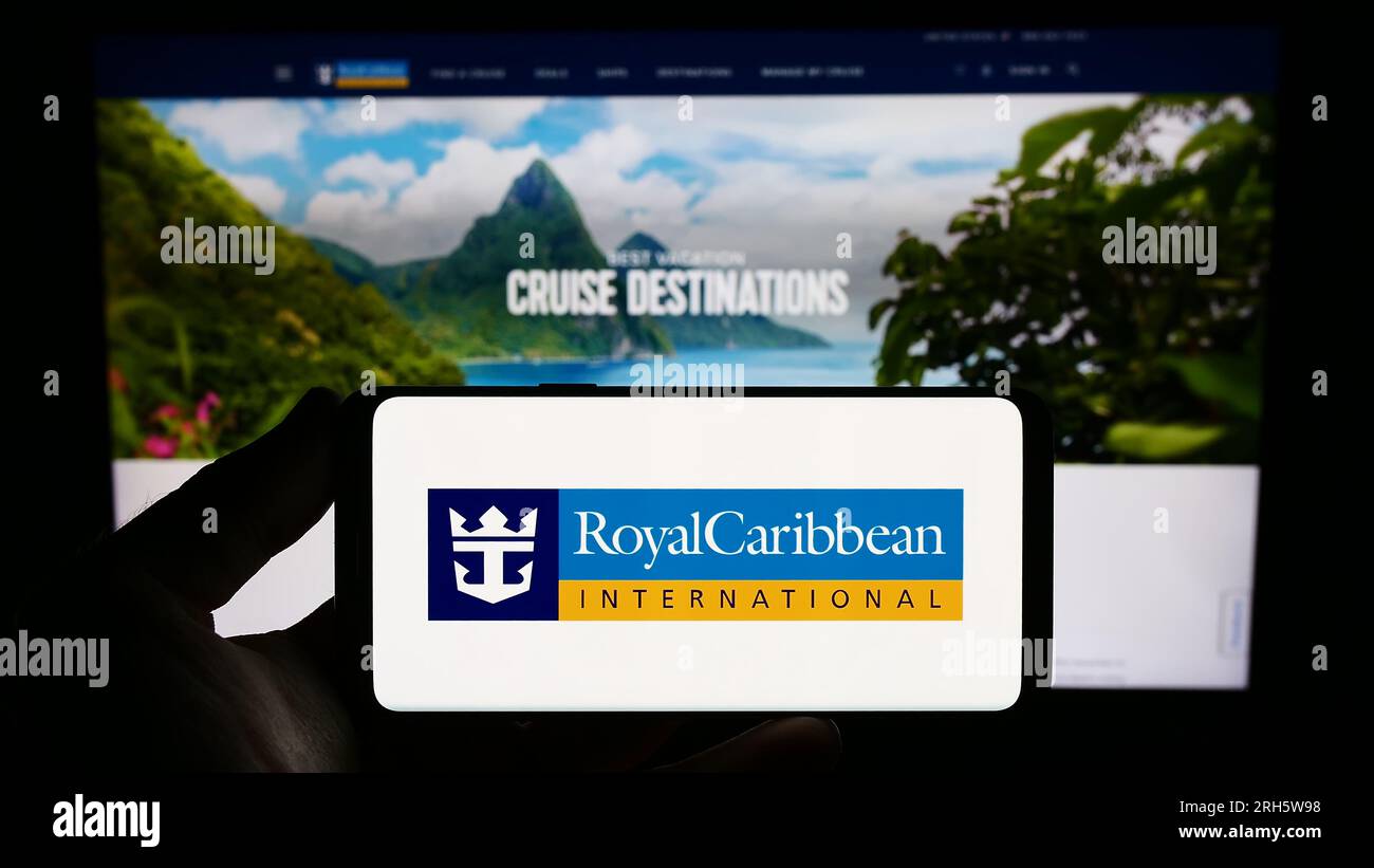 Person holding smartphone with logo of company Royal Caribbean International (RCI) on screen in front of website. Focus on phone display. Stock Photo