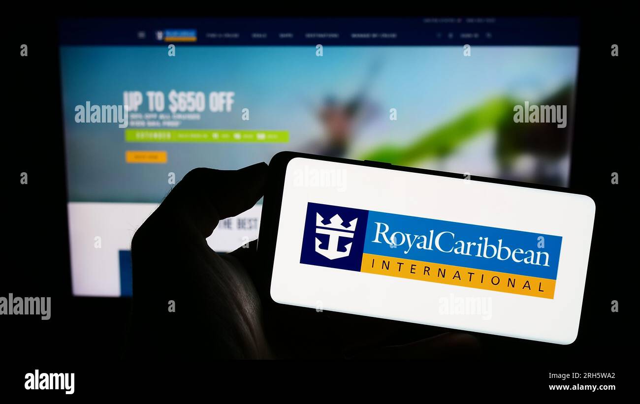Person holding cellphone with logo of company Royal Caribbean International (RCI) on screen in front of business webpage. Focus on phone display. Stock Photo