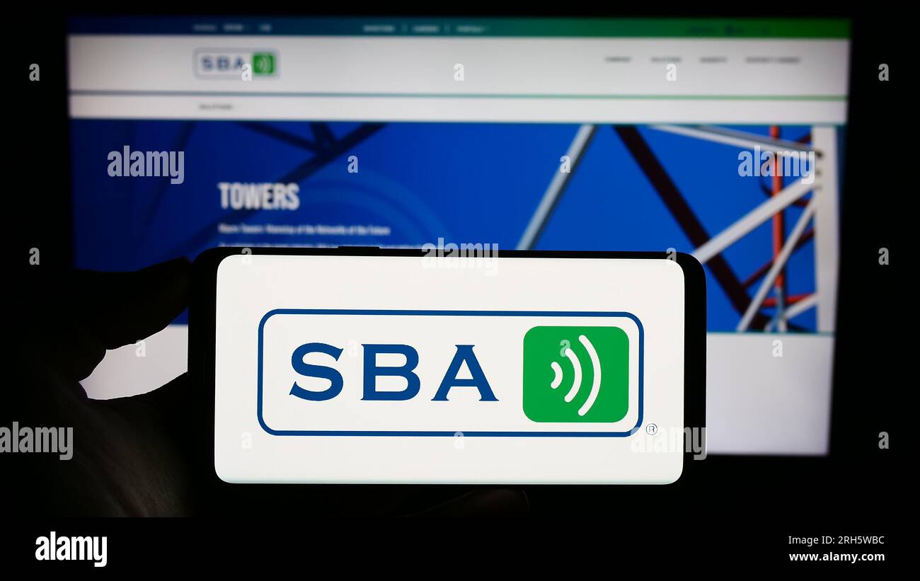 Person holding cellphone with logo of US company SBA Communications Corporation on screen in front of business webpage. Focus on phone display. Stock Photo
