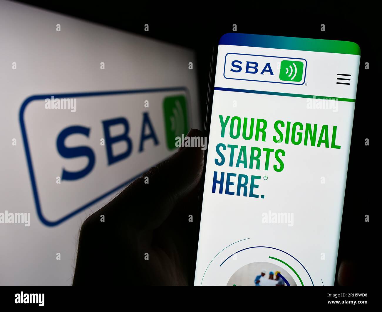 Person holding cellphone with webpage of US company SBA Communications Corporation on screen in front of logo. Focus on center of phone display. Stock Photo