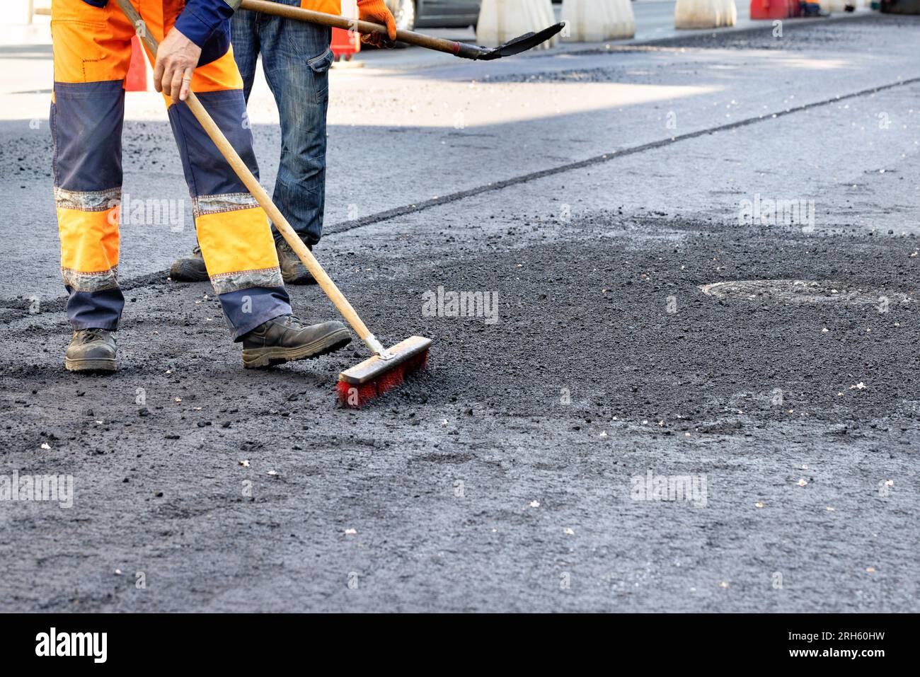 Road workers remove excess rubble with a brush and shovel on the new asphalt surface around the sewer manholes. Copy space. Stock Photo
