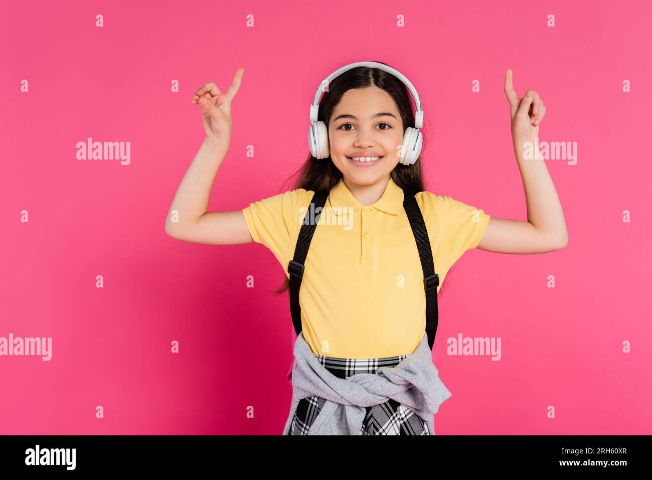 positive girl in wireless headphones showing v sign on pink background ...