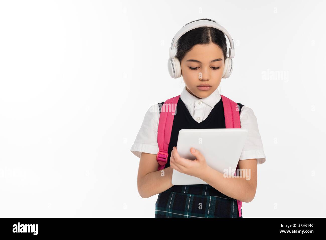 focused schoolgirl in wireless headphones using digital tablet isolated on white, digital age Stock Photo