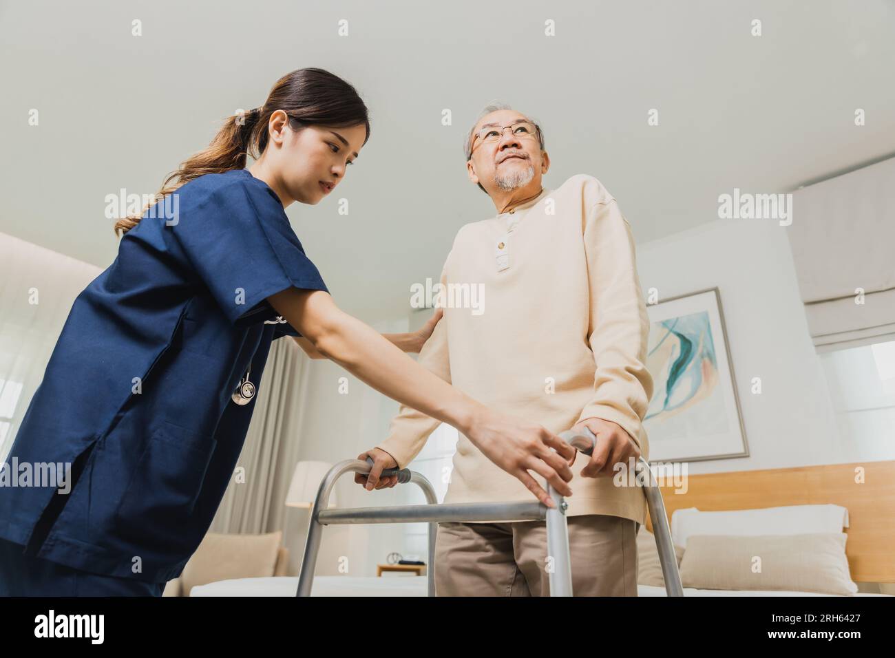 Smiling nurse woman helping senior Asian man to walk around the nursing