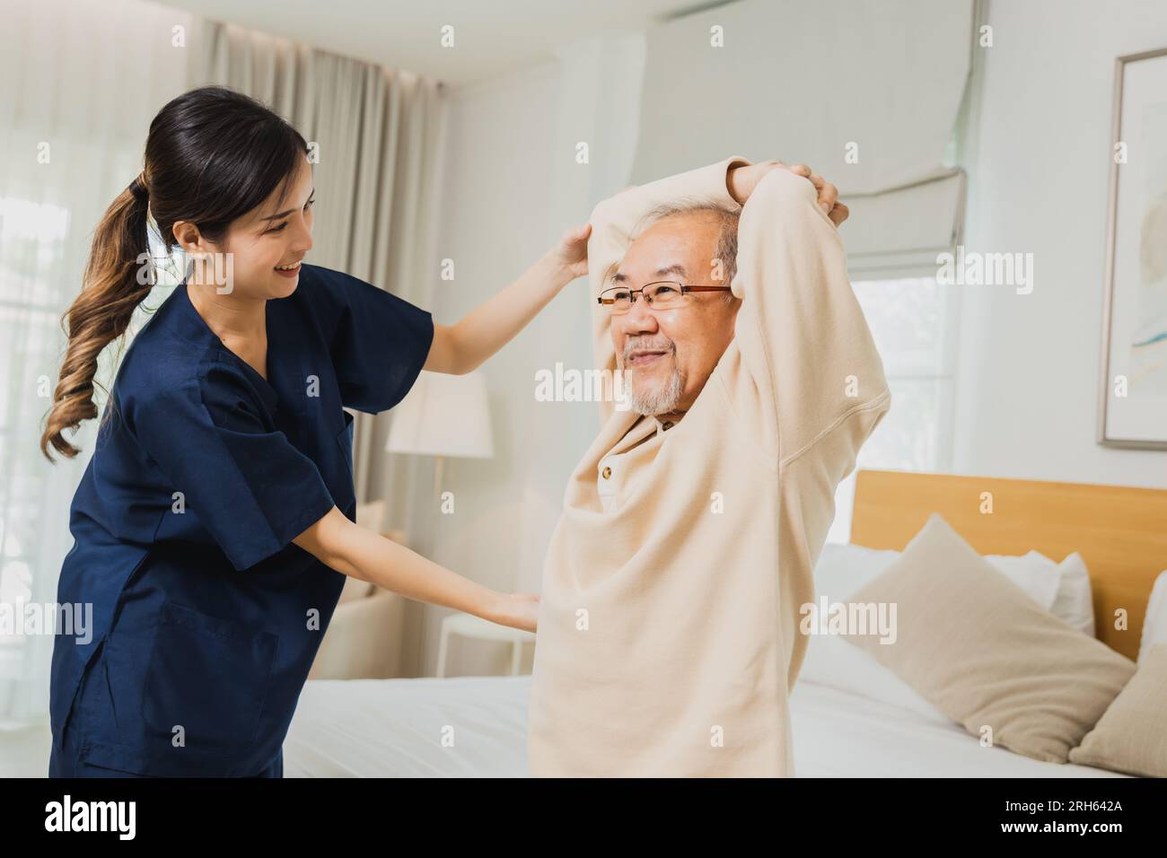 Asian nurse woman assisting old man warming up exercises for the upper body inside the nursing home, use walker with strong health and Help and care c Stock Photo