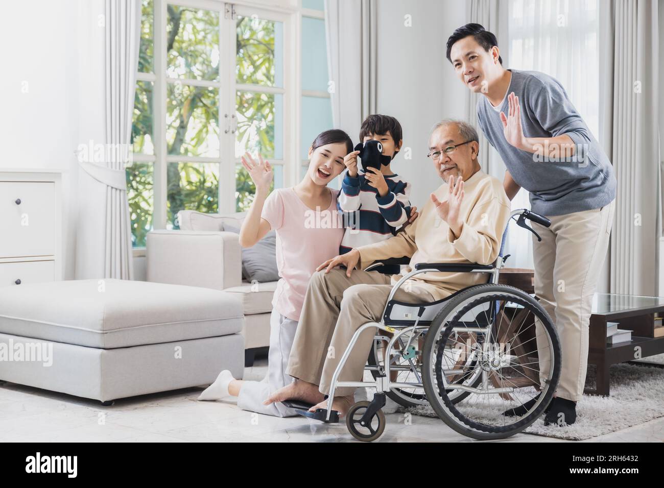 Happy Asian family of senior with beautiful daughter, her husband and grandson take care old man sitting on wheelchair in house, positive dad have str Stock Photo