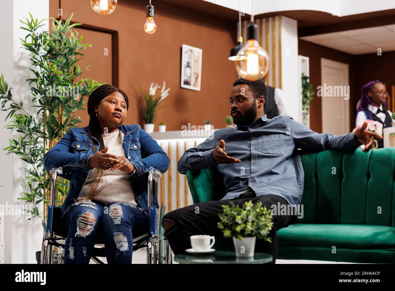 Young African American man and his disabled wife sitting in hotel lobby ...