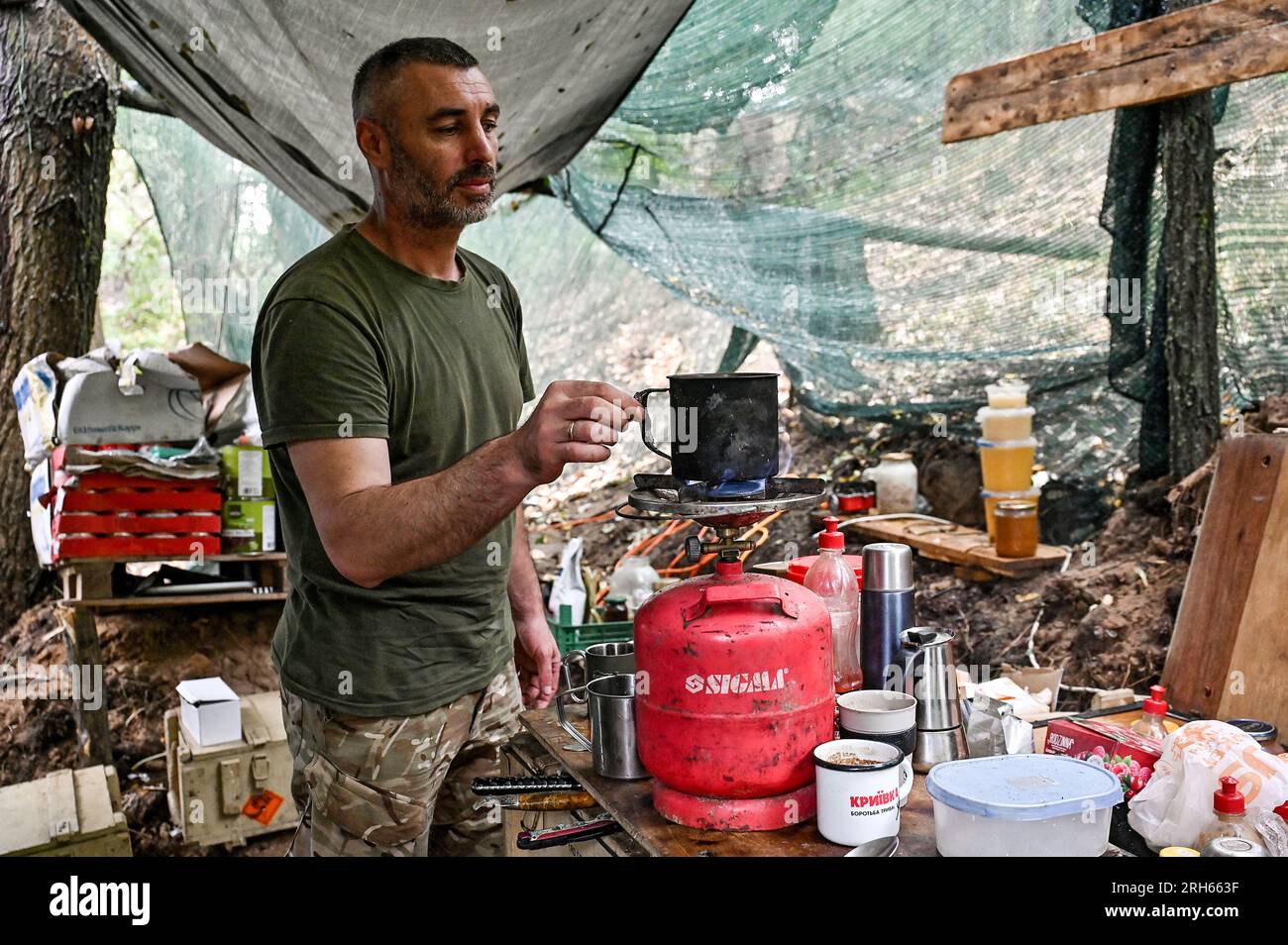 UKRAINE - AUGUST 11, 2023 - A serviceman keeps a mug over a gas cylinder in the field kitchen as the artillery unit of the 128th Mountain Assault Brig Stock Photo