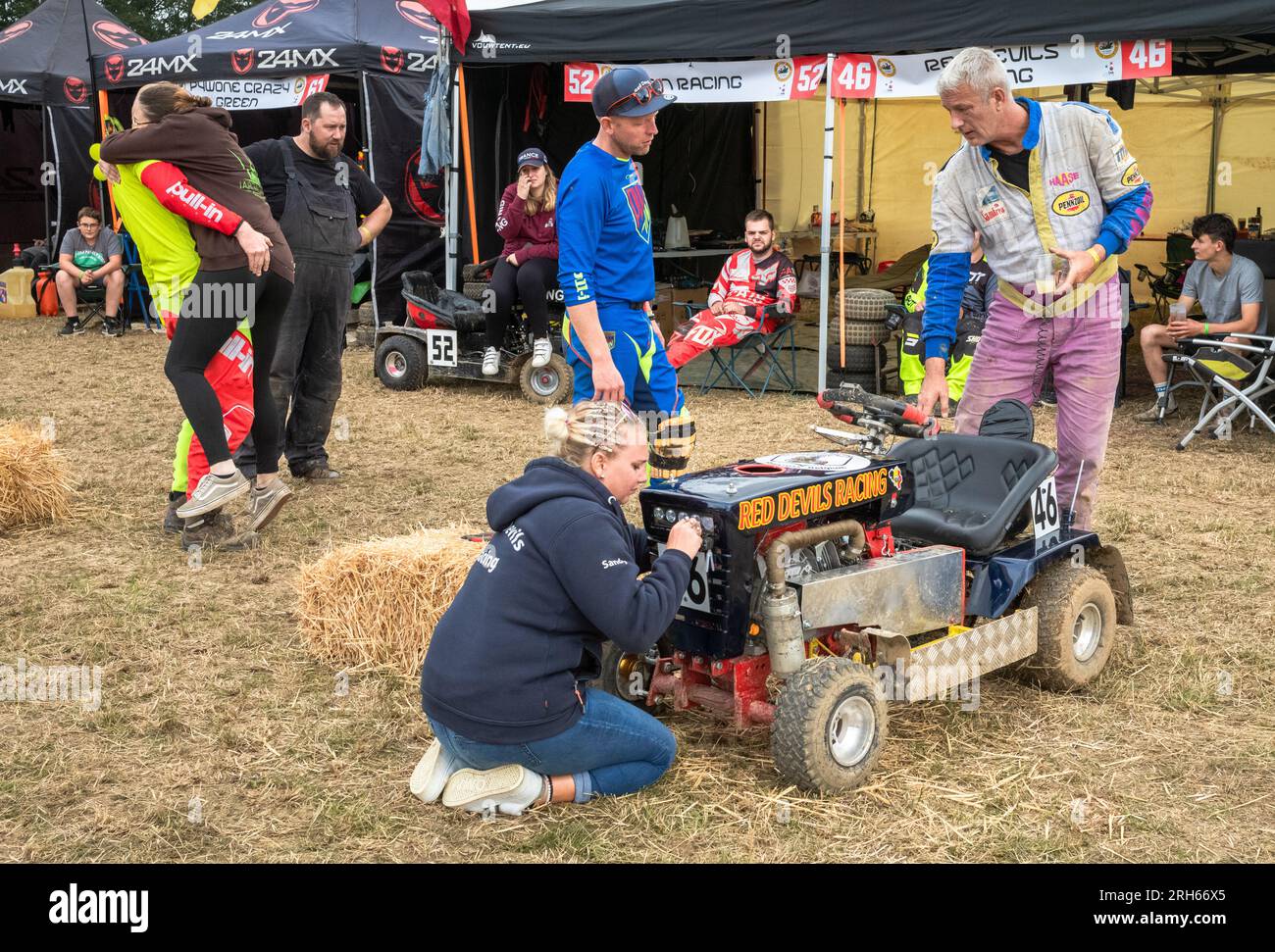 A couple embraces as  members of the 'Red Devils Racing' lawn mower racing team prepare their mower before the annual 14-hour endurance British Lawn M Stock Photo