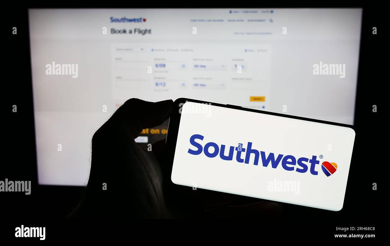 Person holding cellphone with logo of US airline company Southwest Airlines Co. on screen in front of business webpage. Focus on phone display. Stock Photo