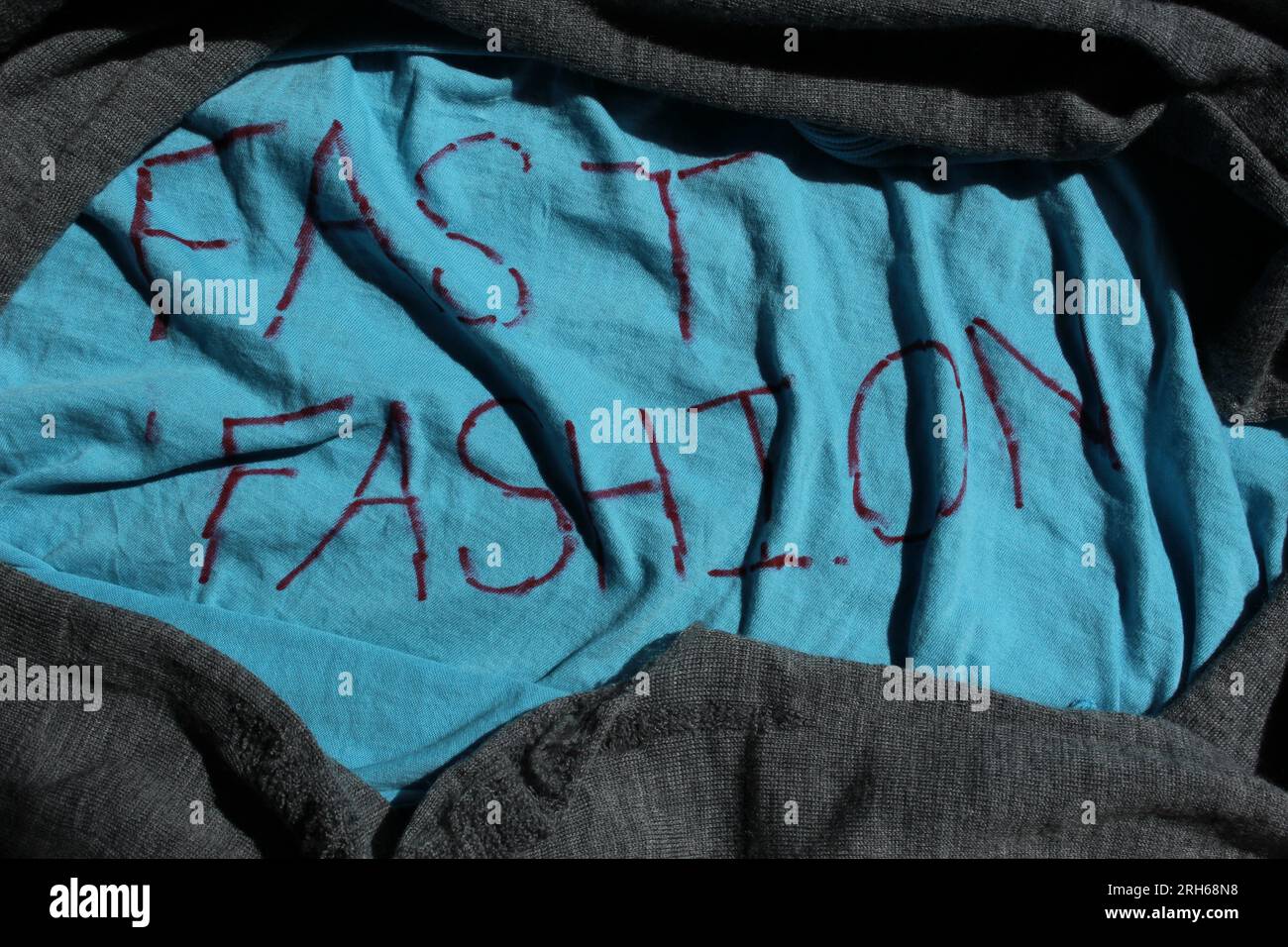 FAST FASHION written on blue textile with other textiles framing it. Concept for fast fashion, clothing consumption, clothes breaking down Stock Photo