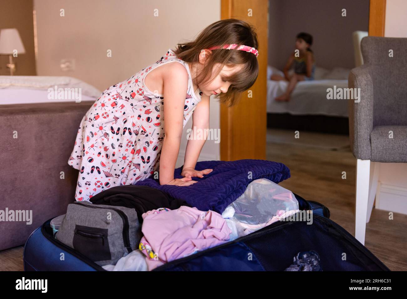 Child girl packing or unpacking suitcase in a hotel room or at home preparing for travel Stock