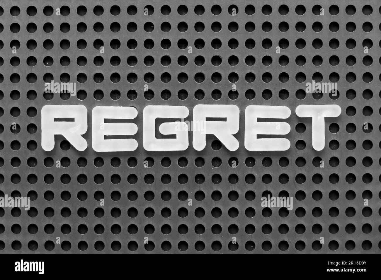 White alphabet letter in word regret on black pegboard background Stock Photo
