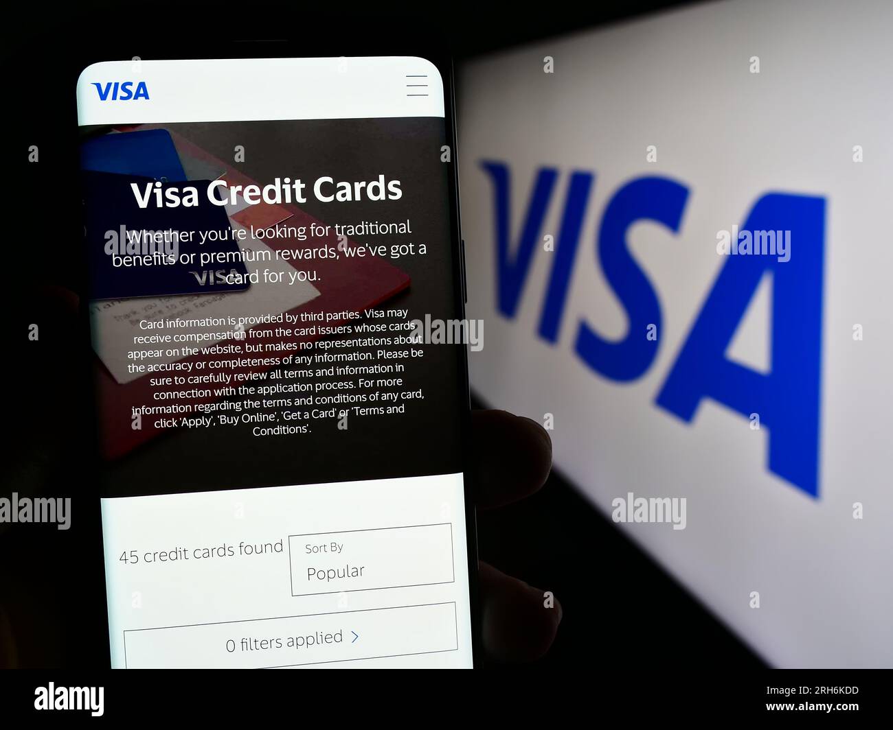 Person holding mobile phone with web page of US payment processing company Visa Inc. on screen in front of logo. Focus on center of phone display. Stock Photo