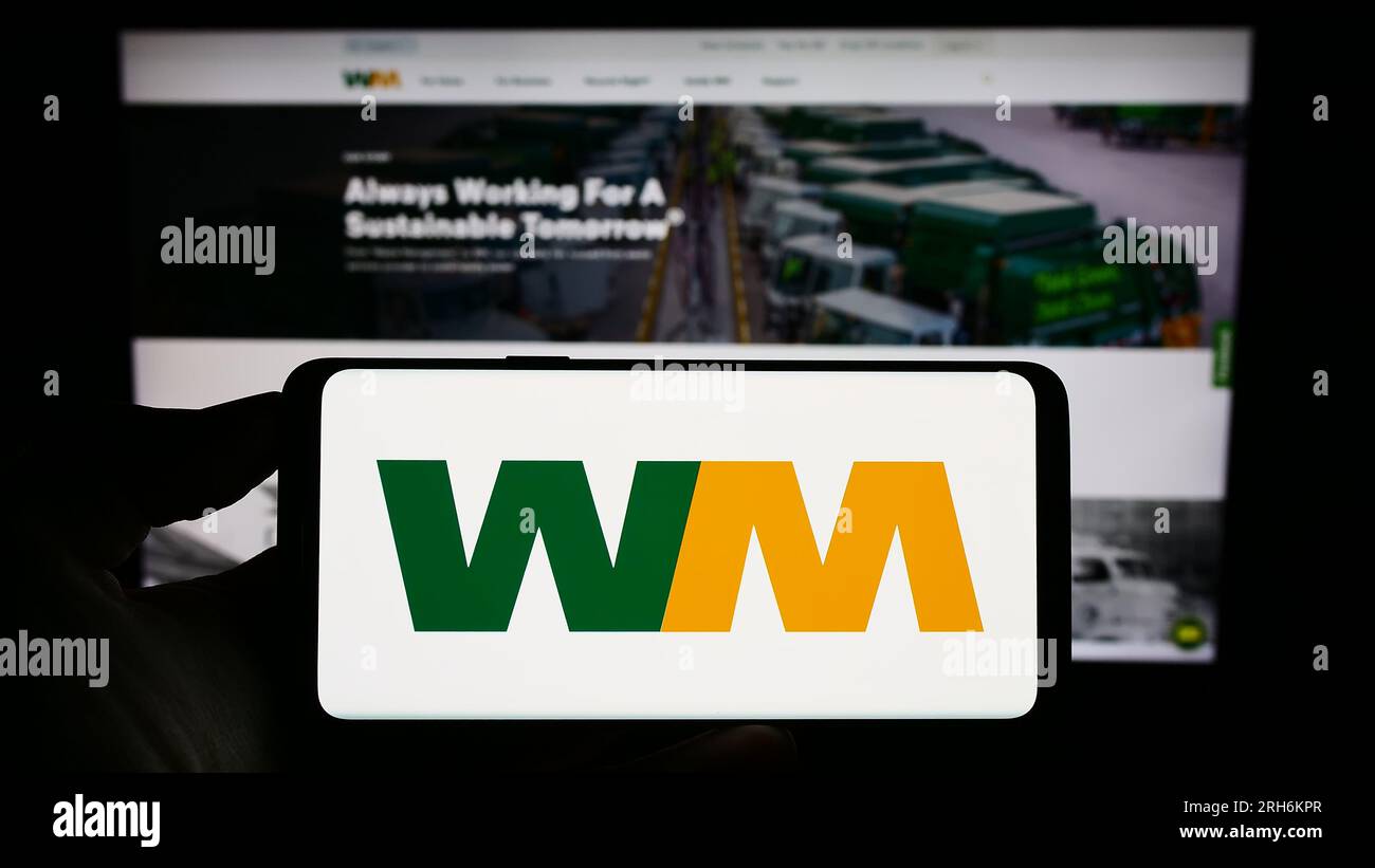 Person holding cellphone with logo of US disposal company Waste Management Inc. on screen in front of business webpage. Focus on phone display. Stock Photo