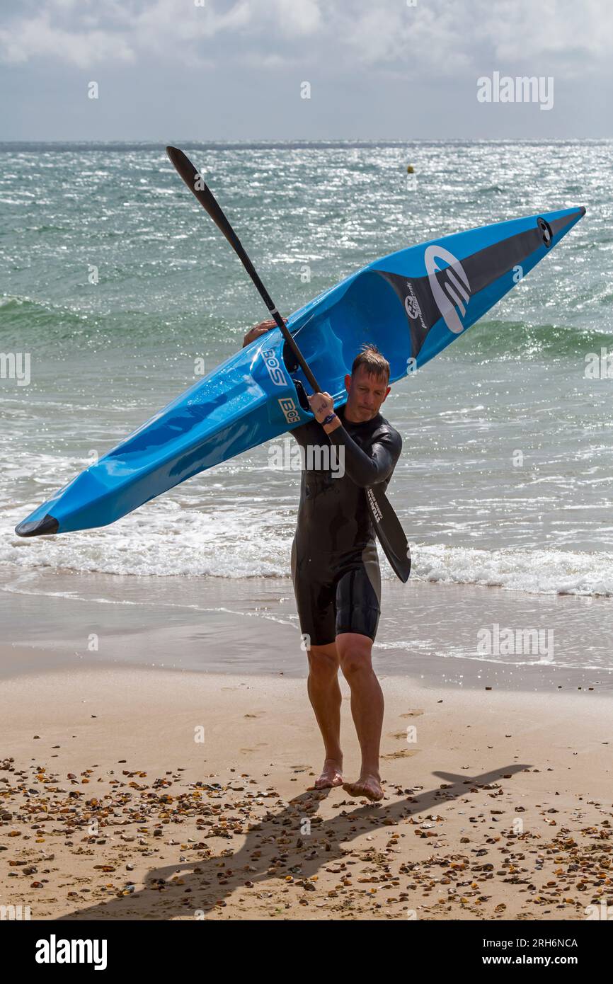 Man carrying BOS Tomahawk surfski surf ski ready up the beach at Branksome Chine beach, Poole, Dorset, UK in August Stock Photo