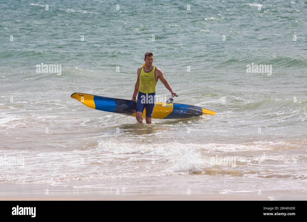 Man carrying surfski surf ski ready up the beach at Branksome Chine beach, Poole, Dorset, UK in August Stock Photo