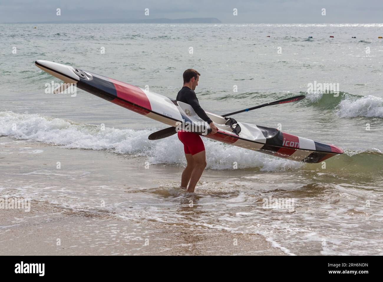 Man getting surfski surf ski ready in the sea to go surf skiing surfskiing at Branksome Chine beach, Poole, Dorset, UK in August Stock Photo