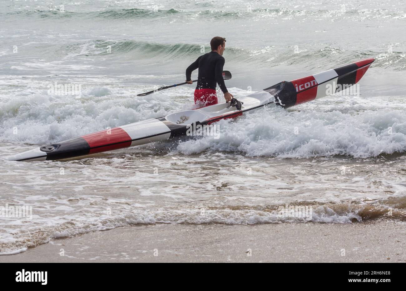 Man getting surfski surf ski ready in the sea to go surf skiing surfskiing at Branksome Chine beach, Poole, Dorset, UK in August Stock Photo