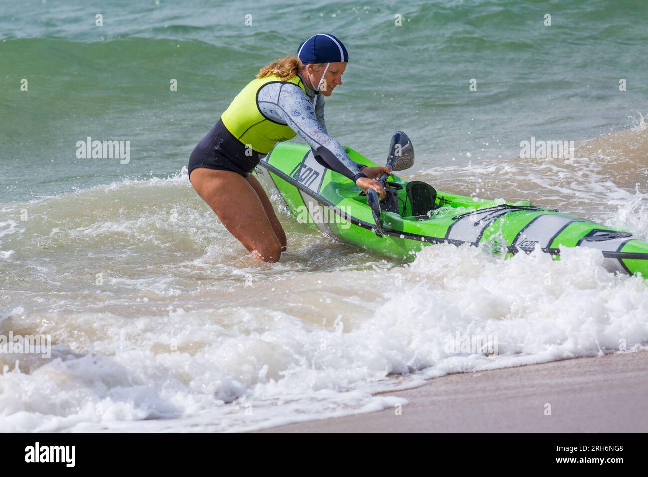 Woman getting surfski surf ski ready in the sea to go surf skiing surfskiing at Branksome Chine beach, Poole, Dorset, UK in August Stock Photo