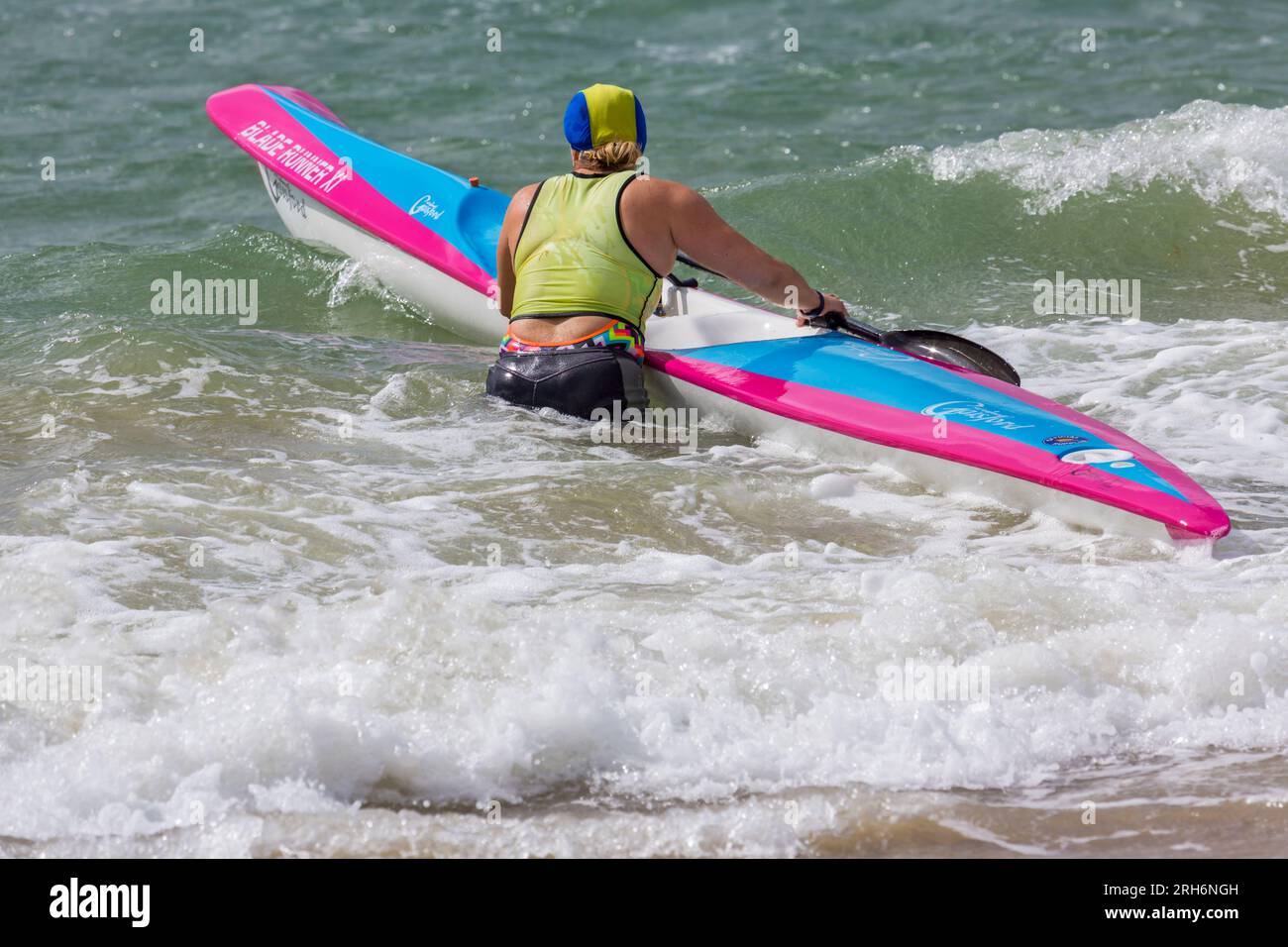 Woman getting surfski surf ski ready in the sea to go surf skiing surfskiing at Branksome Chine beach, Poole, Dorset, UK in August Stock Photo