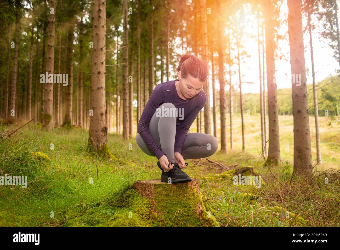 Sporty woman tying up her shoelaces in preperation for running in the forest. Outdoor fitness concept. Stock Photo