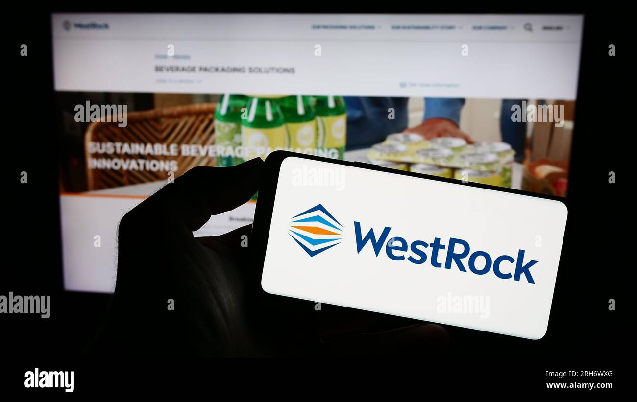 Person holding mobile phone with logo of American packaging business WestRock Company on screen in front of web page. Focus on phone display. Stock Photo