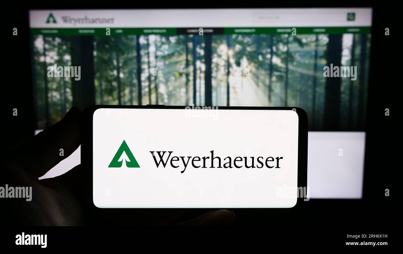 Person holding smartphone with logo of US timberland business Weyerhaeuser Company on screen in front of website. Focus on phone display. Stock Photo